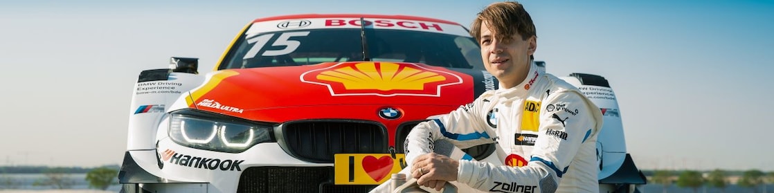 a person sitting on the ground with a jug of oil in front of a race car