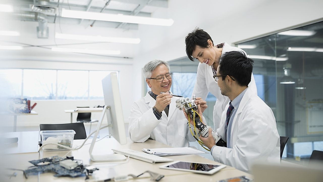 Three people wearing white lab coats talking