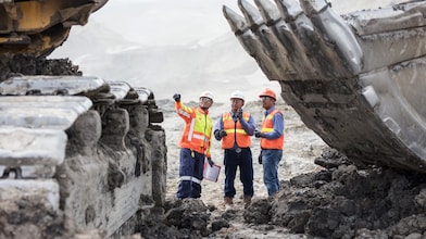 a group of men in orange vests and helmets standing in dirt