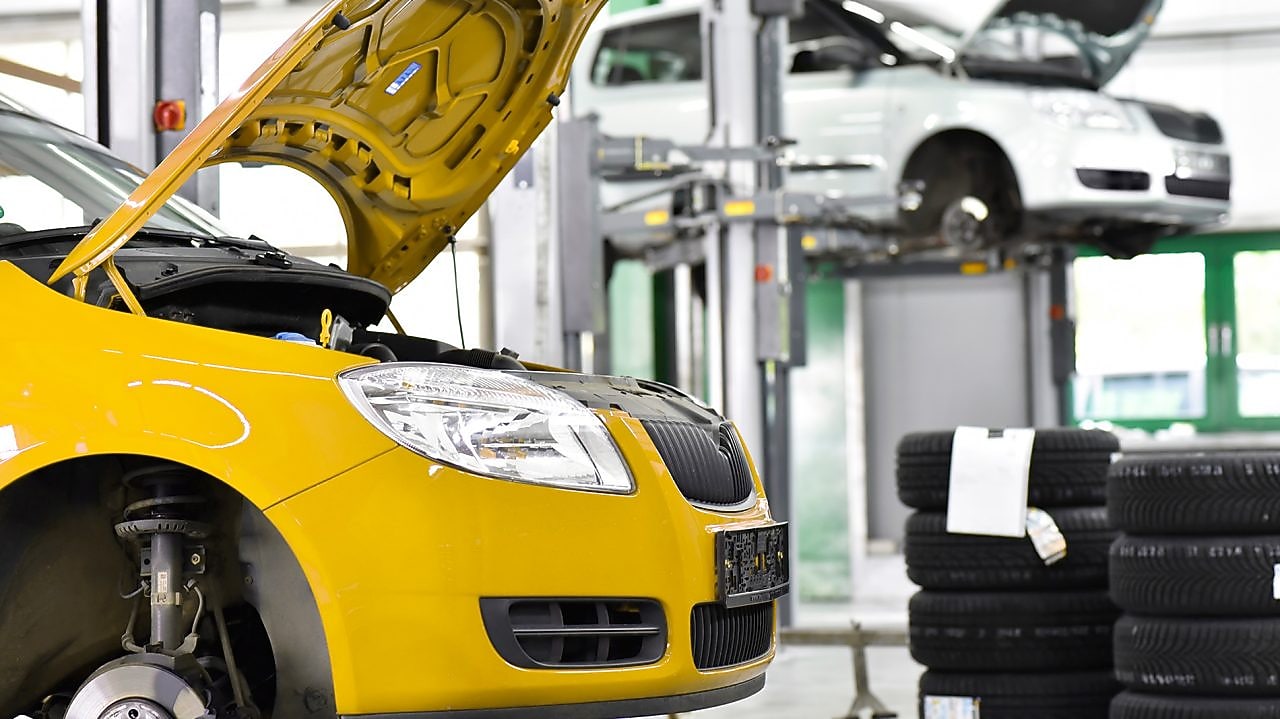 two cars in a garage, one yellow and one white, with their bonnets open, and some car tyres in the background