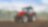  A red tractor ploughing a muddy field with trees in the background