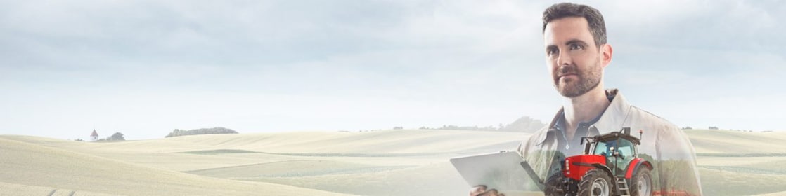 man reading a document with a background of fields and a red tractor