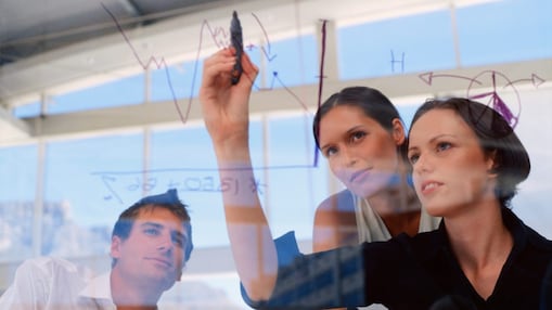 two women and a man are having a team meeting and looking at a graph on a white board
