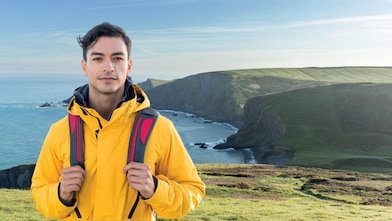Young man standing on cliff side overlooking a calm sea