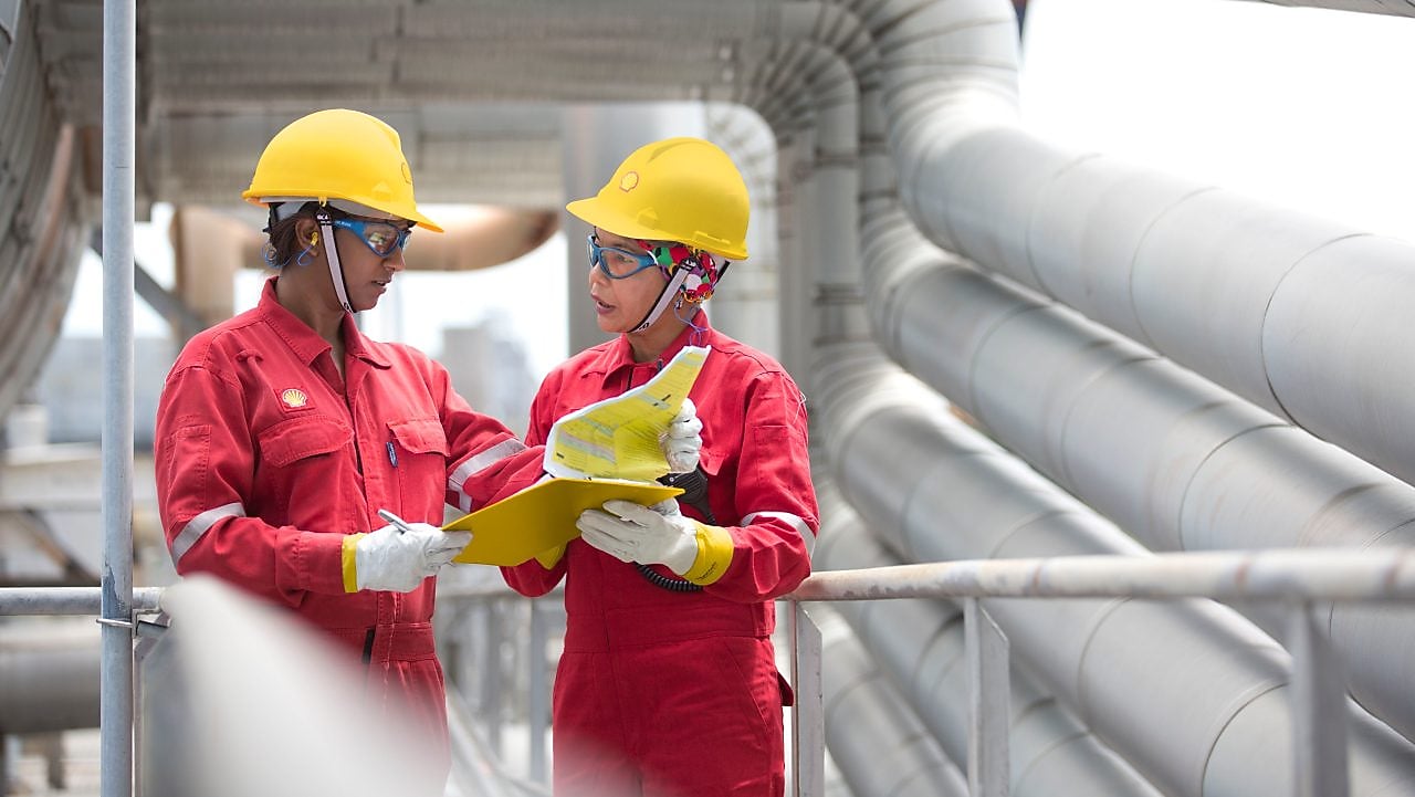 Shot of two workers in hardhats discussing a project in a refinery