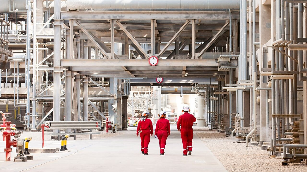 Three engineers walking on site through a refinery
