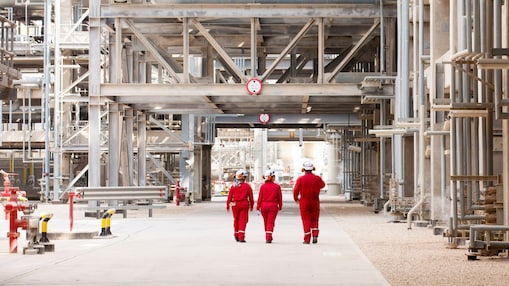 Three engineers walking on site through a refinery