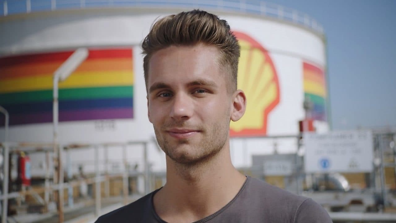 A male Shell employee standing in front of a refinery with rainbow colors