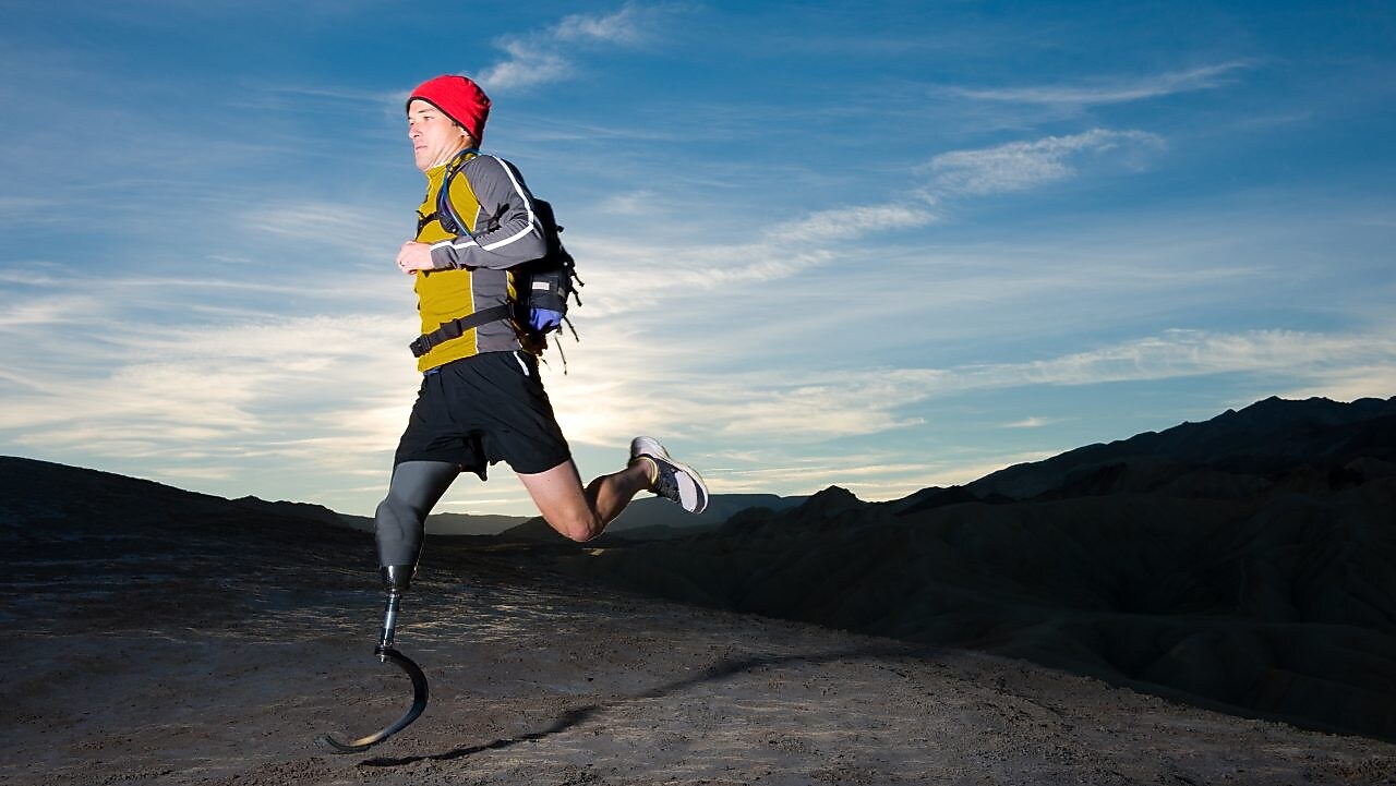man with prosthetic leg, in running clothes, running in the hills in the early morning