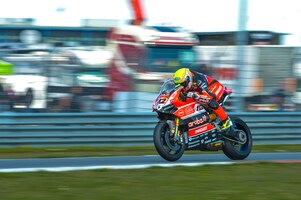 Ducati superbike with rider racing on a track with lorries in the background