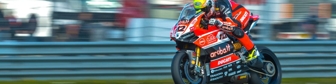 Ducati superbike with rider racing on a track with lorries in the background