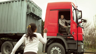 Man in red truck cab with door open waving to his daughter