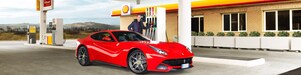 A red Ferrari sitting on a Shell station forecourt with a man leaning on a petrol pump