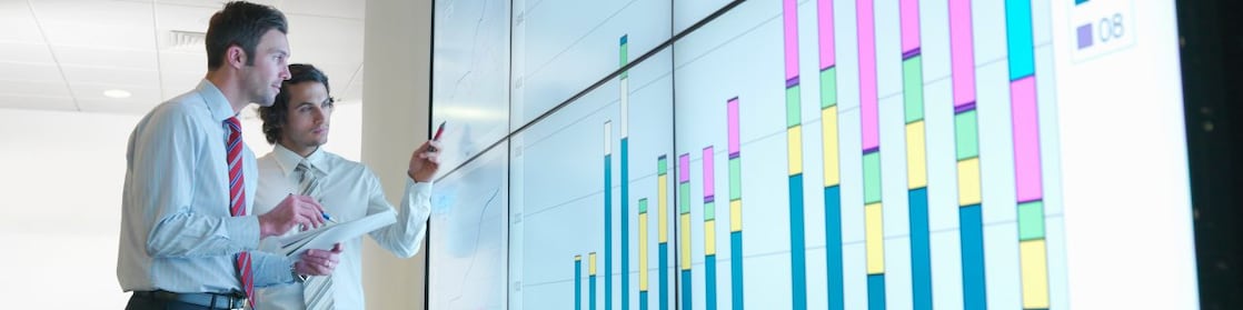 Business men analyse reports displayed on a large digital screen