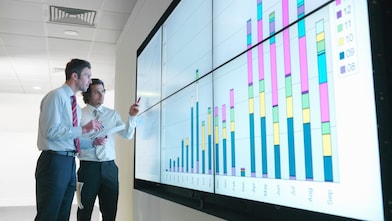 Business men analyse reports displayed on a large digital screen